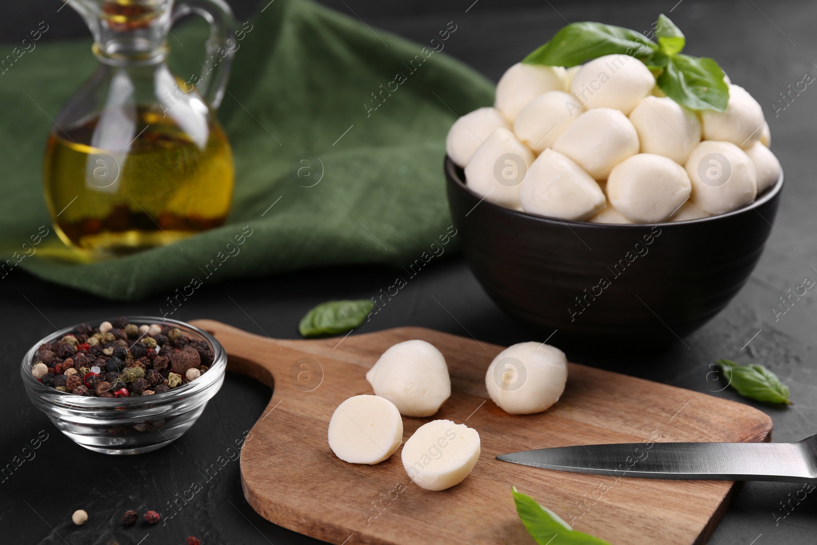 Photo of Tasty mozzarella balls, basil leaves and spices on black table