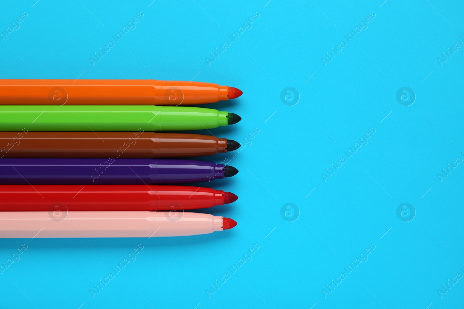 Photo of Many different colorful markers on light blue background, flat lay. Space for text