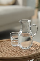 Photo of Jug and glass with clear water on wicker surface against blurred background