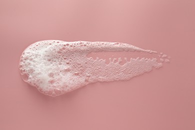 Photo of Smudge of white washing foam on pale pink background, top view