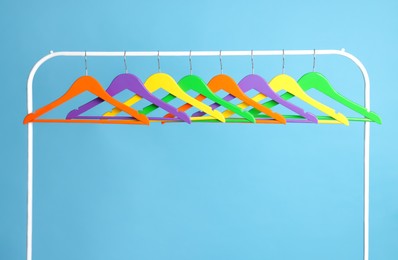 Photo of Bright clothes hangers on metal rack against light blue background
