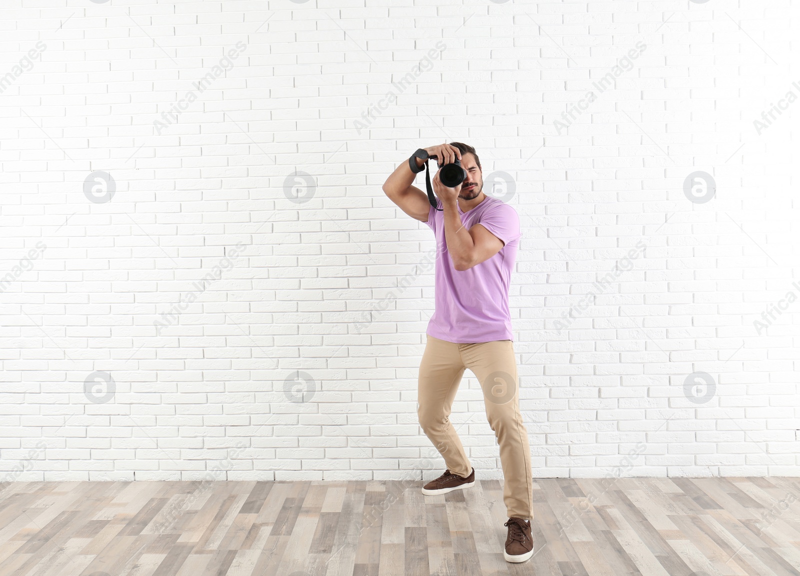 Photo of Young professional photographer taking picture near brick wall. Space for text