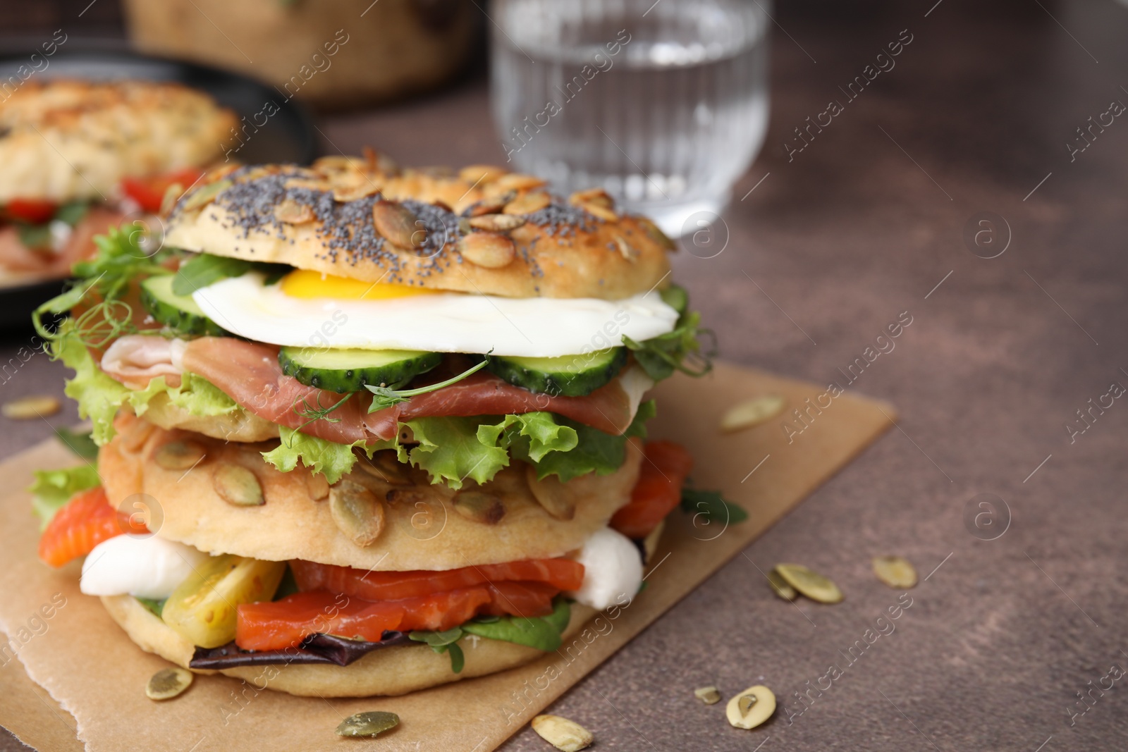 Photo of Tasty bagel with cured ham, egg, salmon and vegetables on brown table, closeup. Space for text