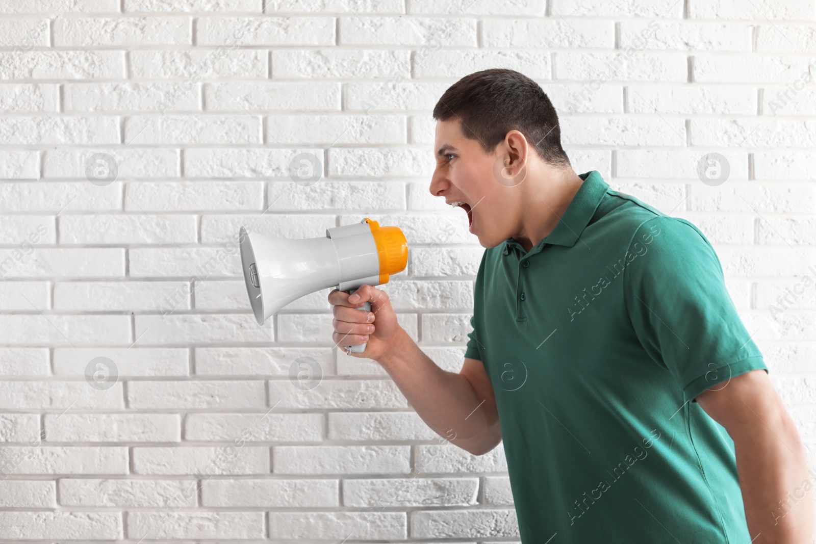 Photo of Portrait of young man using megaphone near brick wall. Space for text