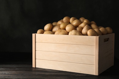 Photo of Raw fresh organic potatoes on wooden table against dark background