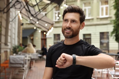 Photo of Handsome bearded man checking time in outdoor cafe