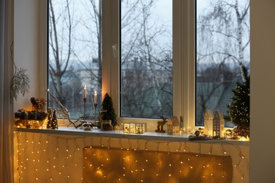 Many beautiful Christmas decorations, candlesticks and festive lights on window sill indoors