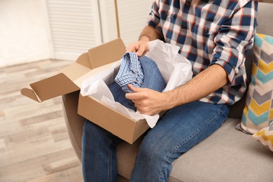 Young man opening parcel at home, closeup