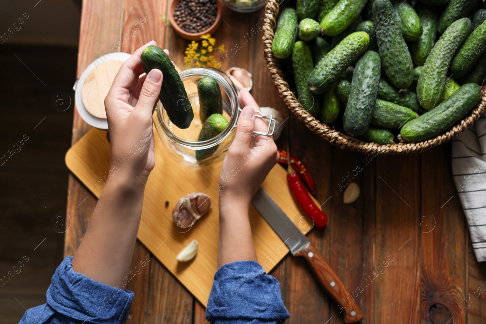 Photo of Woman putting cucumbers into jar at wooden table, top view. Pickling vegetables