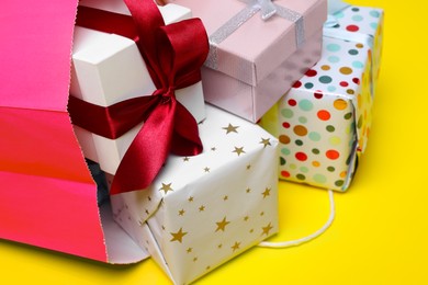 Pink paper shopping bag full of gift boxes on yellow background, closeup