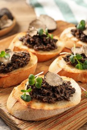 Delicious bruschettas with truffle sauce and microgreens on wooden table, closeup