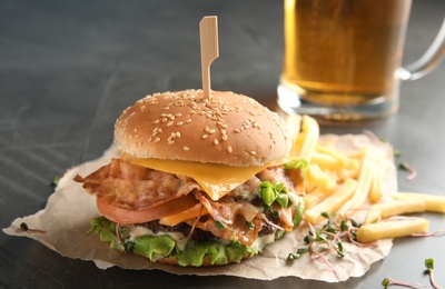 Tasty burger with bacon and French fries on table