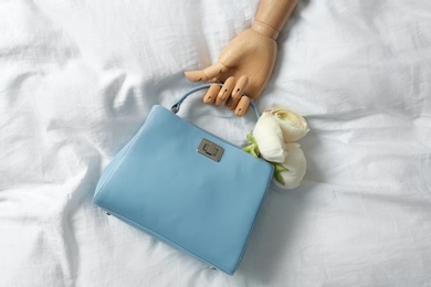 Photo of Stylish bag with spring flowers and wooden mannequin hand on crumpled sheet, flat lay