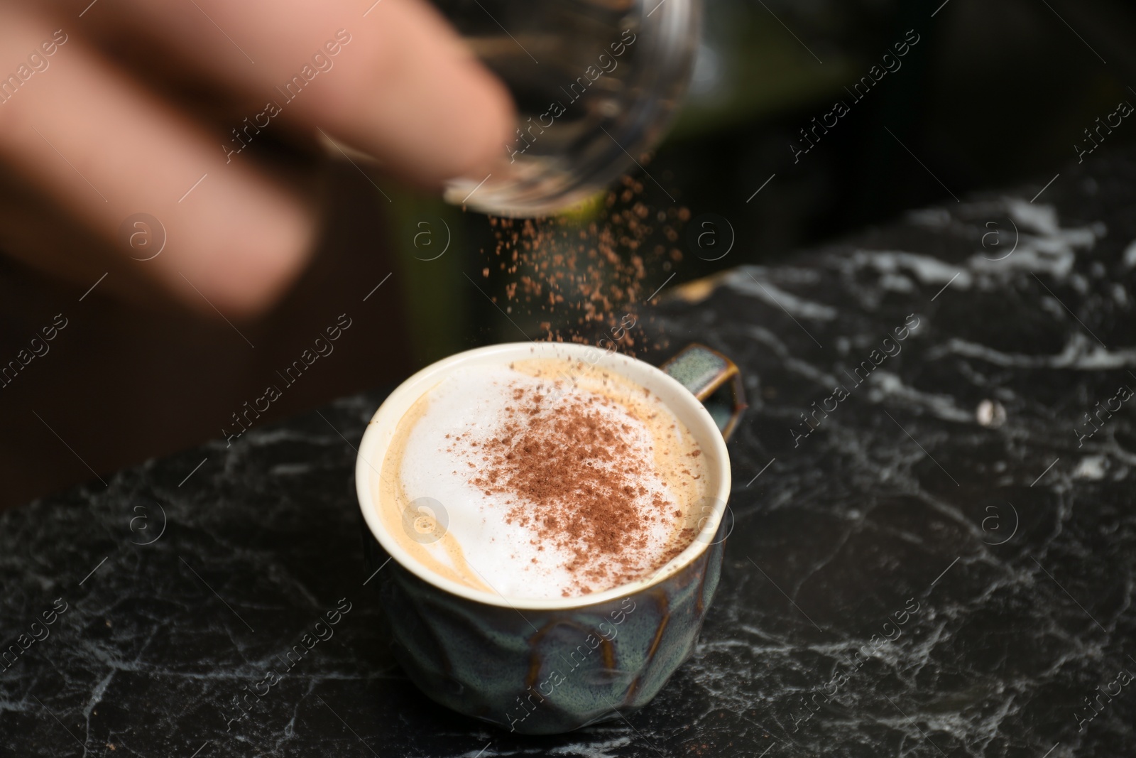 Photo of Barista decorating coffee with cinnamon at table, closeup