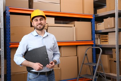 Photo of Young man with clipboard near rack of cardboard boxes at warehouse