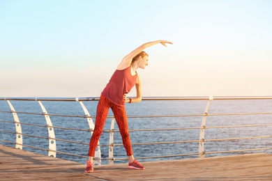 Photo of Young woman doing fitness exercises on pier in morning