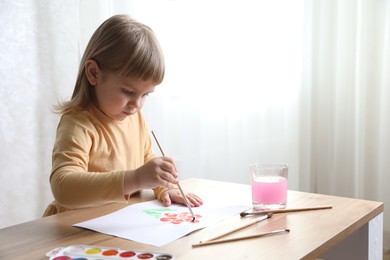 Photo of Cute little girl drawing with brush at wooden table indoors. Child`s art