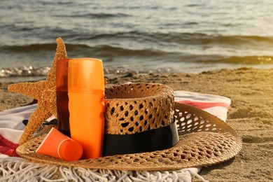 Photo of Sun protection products, hat and starfish on blanket near sea, space for text