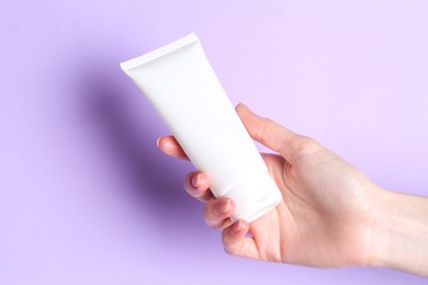 Woman holding tube of cream on violet background, closeup