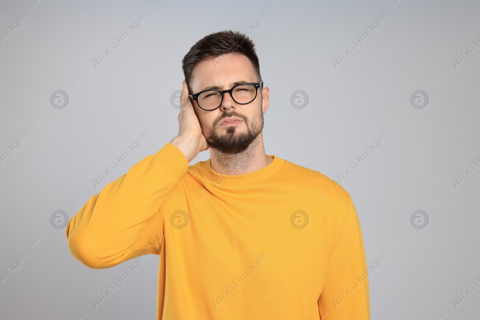 Photo of Young man suffering from ear pain on light grey background