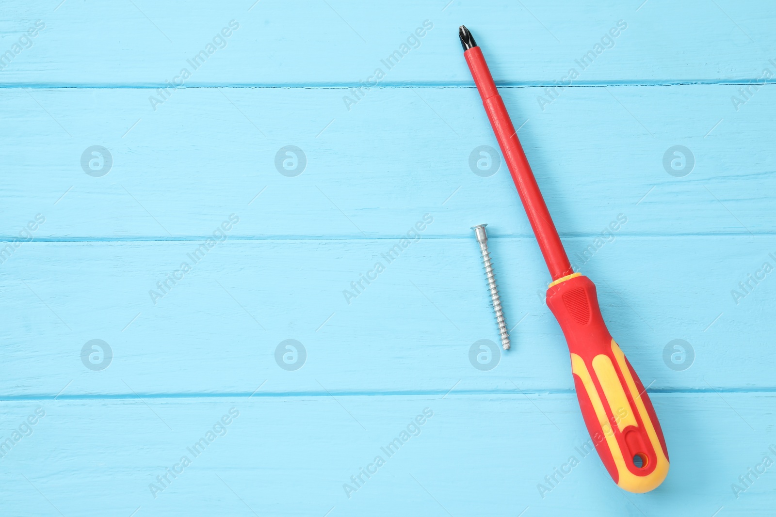 Photo of Screwdriver with red handle and screw on light blue wooden table, flat lay. Space for text