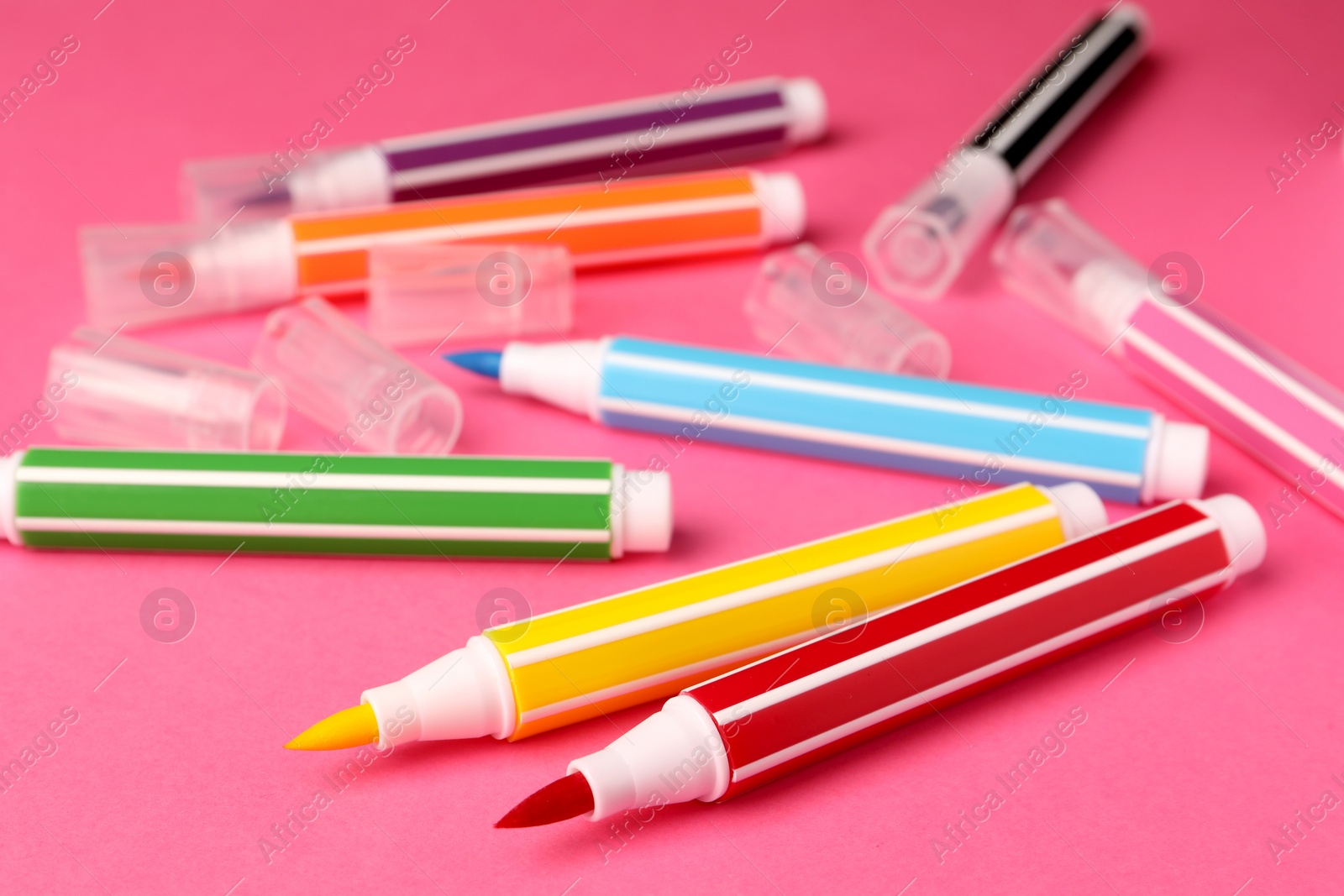 Photo of Many bright markers on pink background, closeup