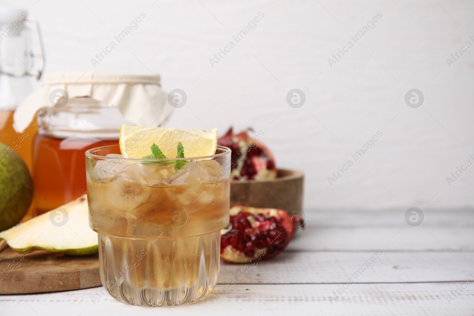 Photo of Tasty kombucha and ice cubes in glass on white wooden table, space for text