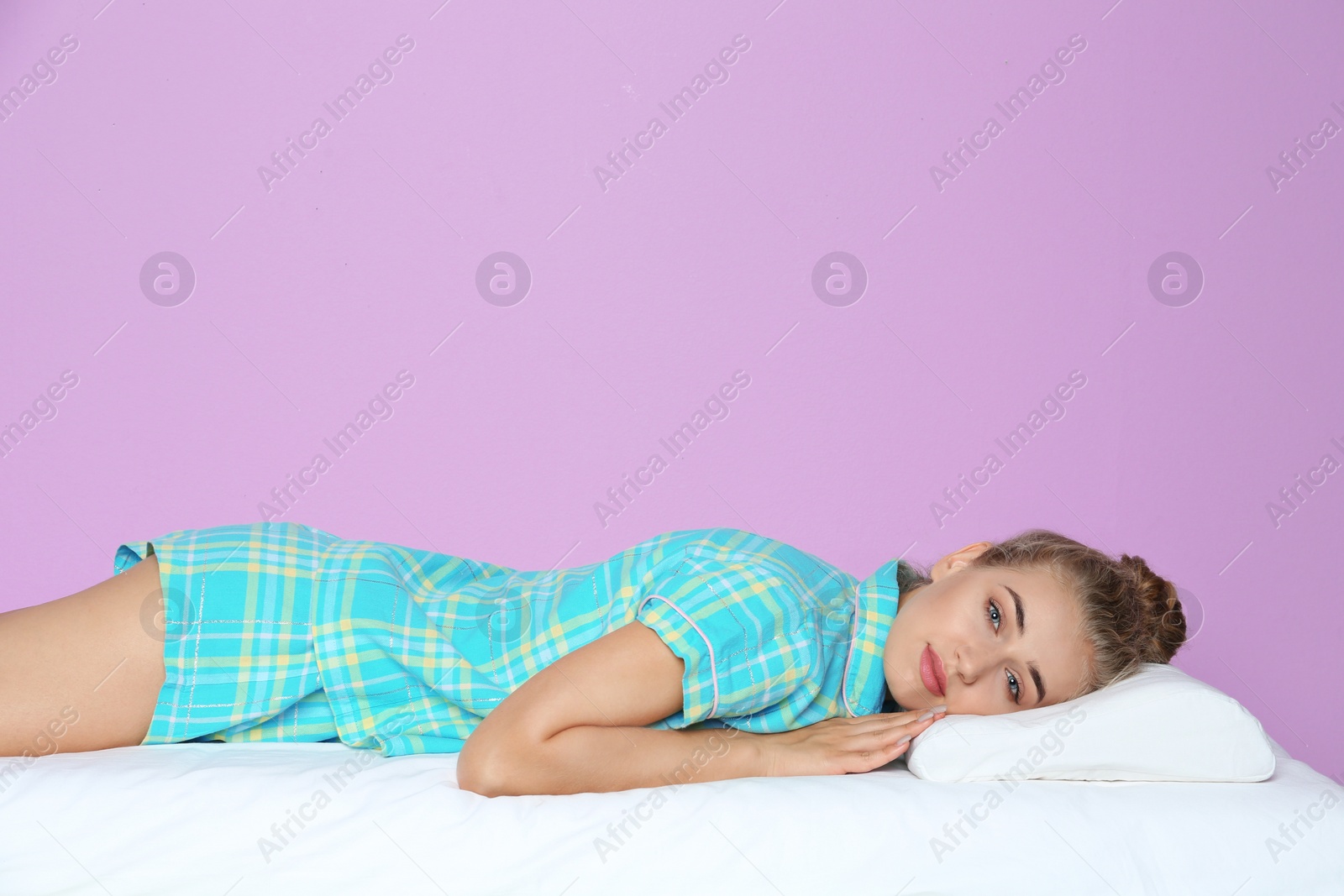 Photo of Beautiful woman lying with orthopedic pillow on bed against color background