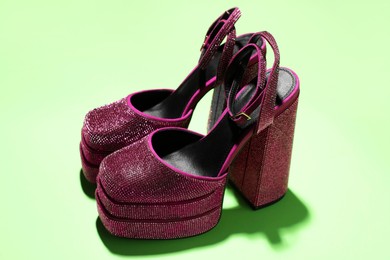 Photo of Fashionable punk square toe ankle strap pumps on green background. Shiny party platform high heeled shoes