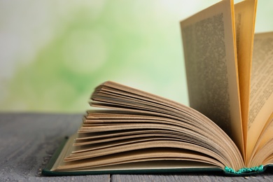 Open book on grey wooden table against blurred green background, closeup