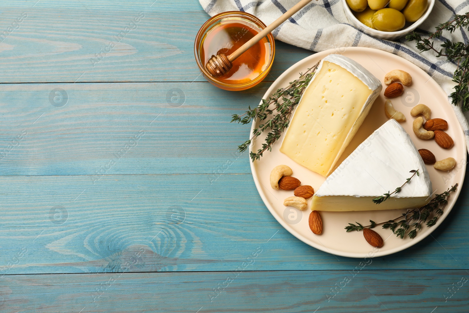 Photo of Tasty Camembert cheese with thyme, honey and nuts on light blue wooden table, flat lay. Space for text