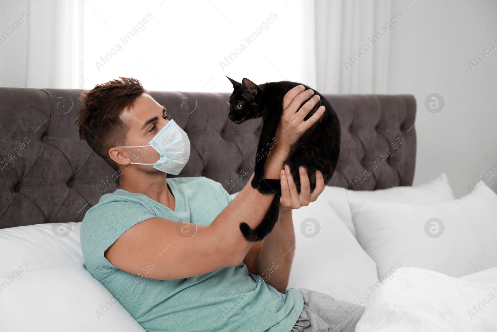 Photo of Young man with cat suffering from allergy in bedroom