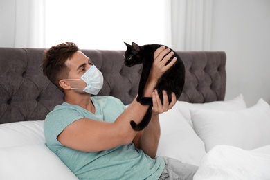 Photo of Young man with cat suffering from allergy in bedroom