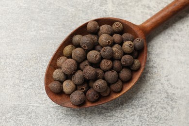 Photo of Aromatic allspice pepper grains in wooden spoon on grey table, top view