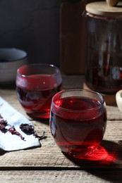 Photo of Delicious hibiscus tea in cups and dry roselle petals on wooden table