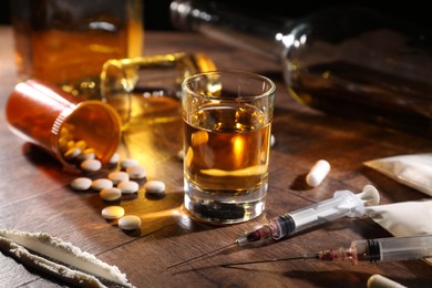 Photo of Alcohol and drug addiction. Whiskey in glass, syringes, pills and cocaine on wooden table