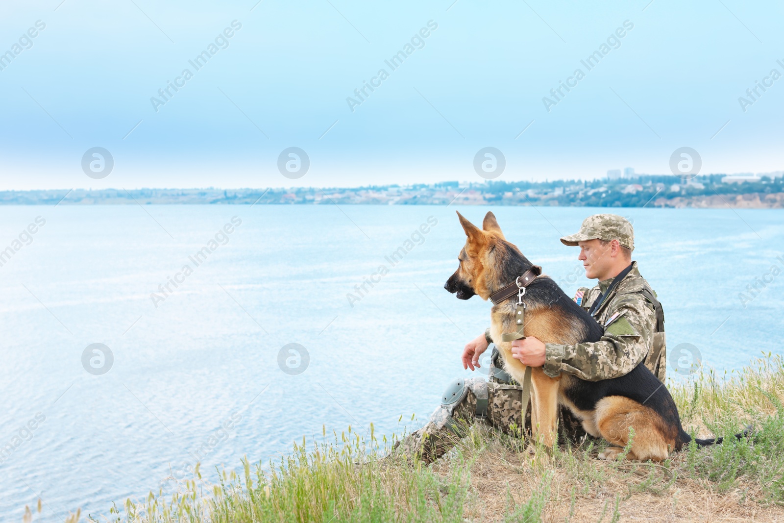 Photo of Man in military uniform with German shepherd dog near river