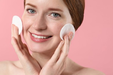 Photo of Smiling woman with freckles wiping face on pink background, closeup