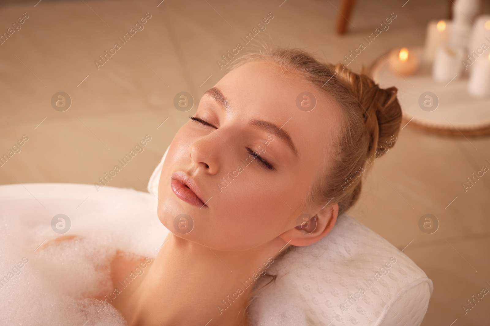 Photo of Young woman using pillow while enjoying bubble bath indoors