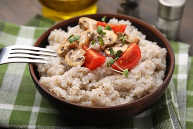 Photo of Delicious barley porridge with mushrooms, tomatoes and microgreens in bowl served on table, closeup