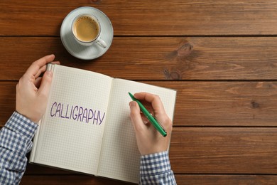 Image of Man writing word Calligraphy in notebook at wooden table, top view. Space for text