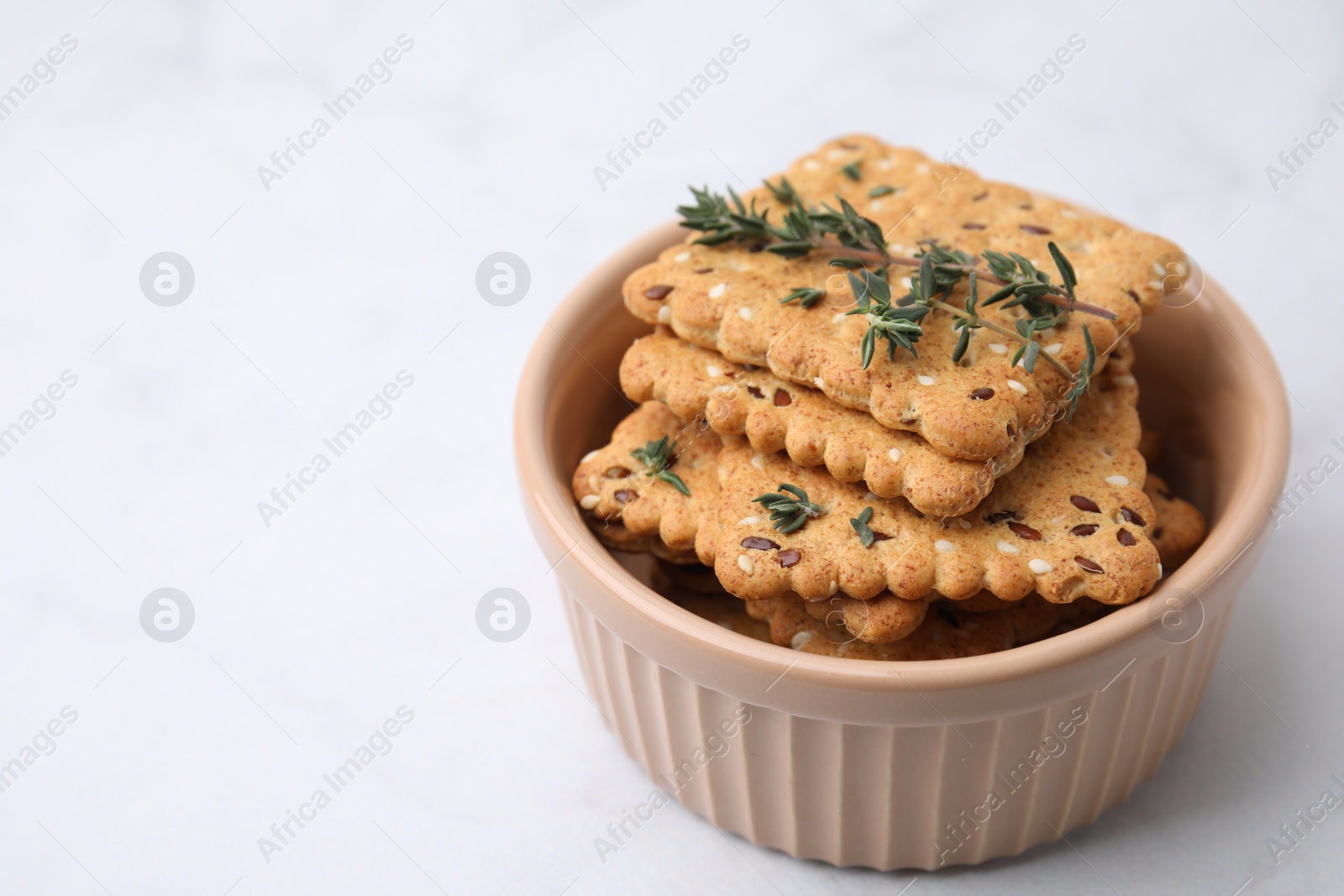 Photo of Cereal crackers with flax, sesame seeds and thyme in bowl on white table, closeup. Space for text