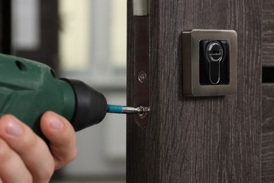 Handyman with drill repairing door lock indoors, closeup