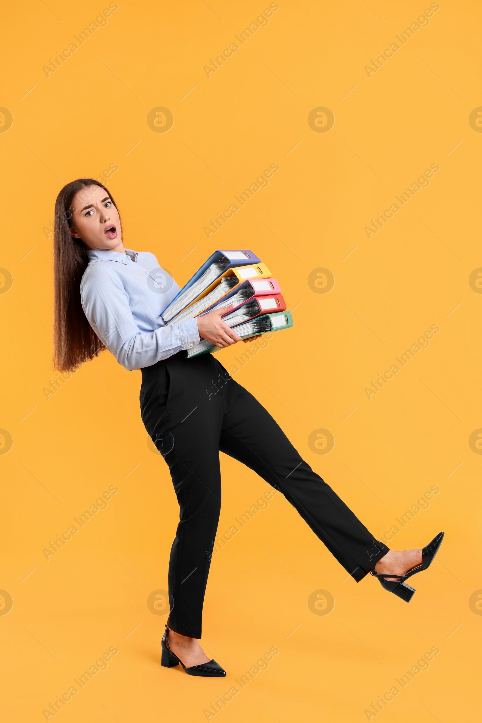 Photo of Shocked woman with folders walking on orange background