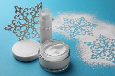 Set of cosmetic products with hand cream and Christmas decor on light blue background, space for text. Winter skin care