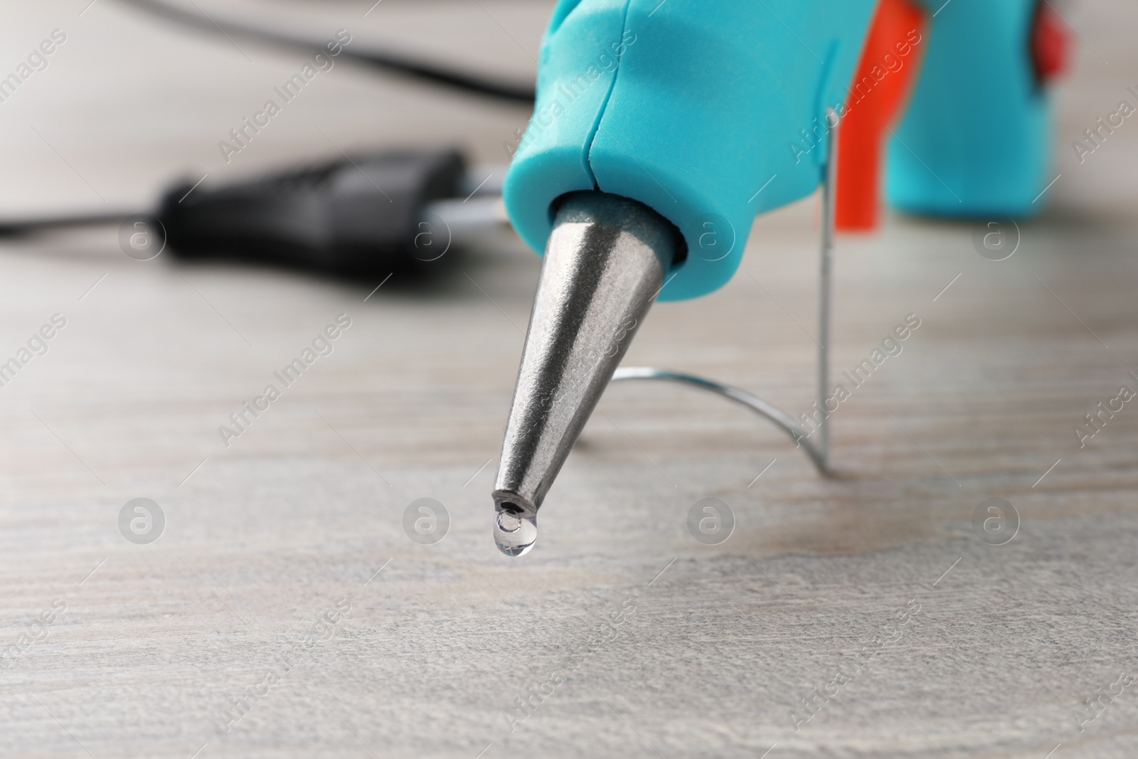 Photo of Melted glue dripping from hot gun on wooden table, closeup