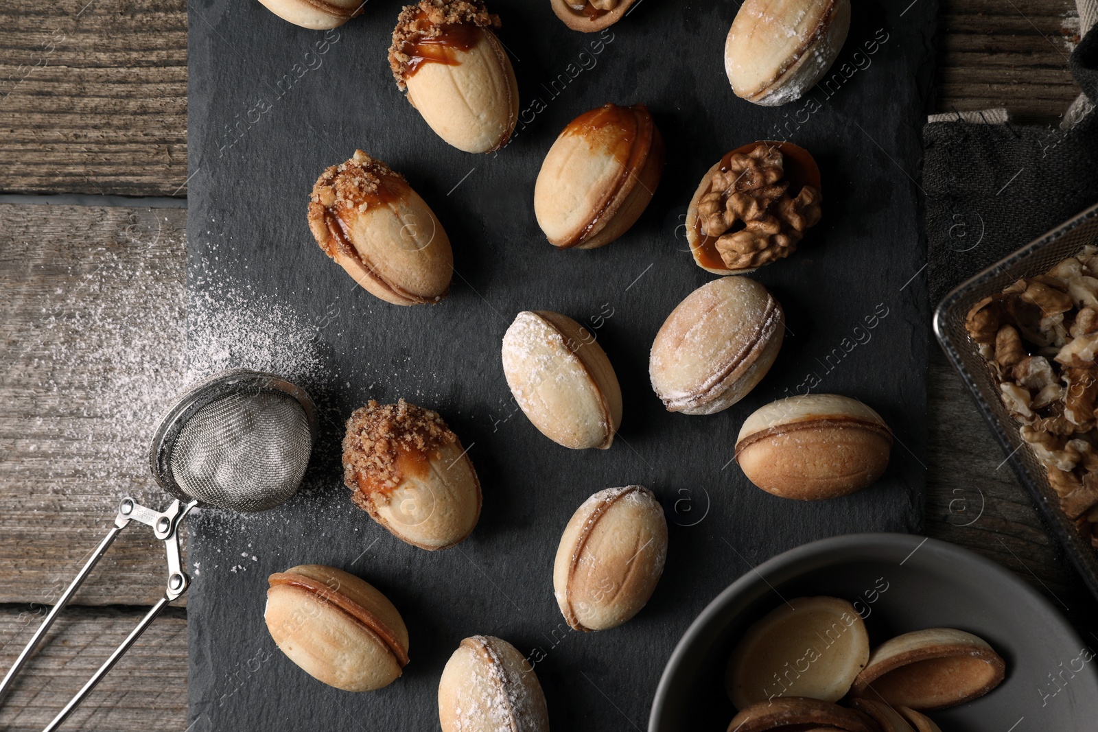 Photo of Freshly baked homemade walnut shaped cookies, nuts and flour on wooden table, flat lay
