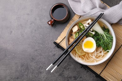 Photo of Bowl of vegetarian ramen, soy sauce and chopsticks on grey table, flat lay. Space for text