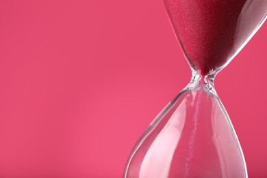 Photo of Hourglass with flowing sand on pink background, closeup. Space for text