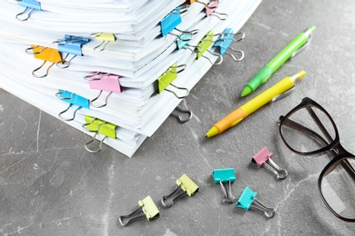 Photo of Stack of documents with binder clips and glasses on grey stone table, closeup view
